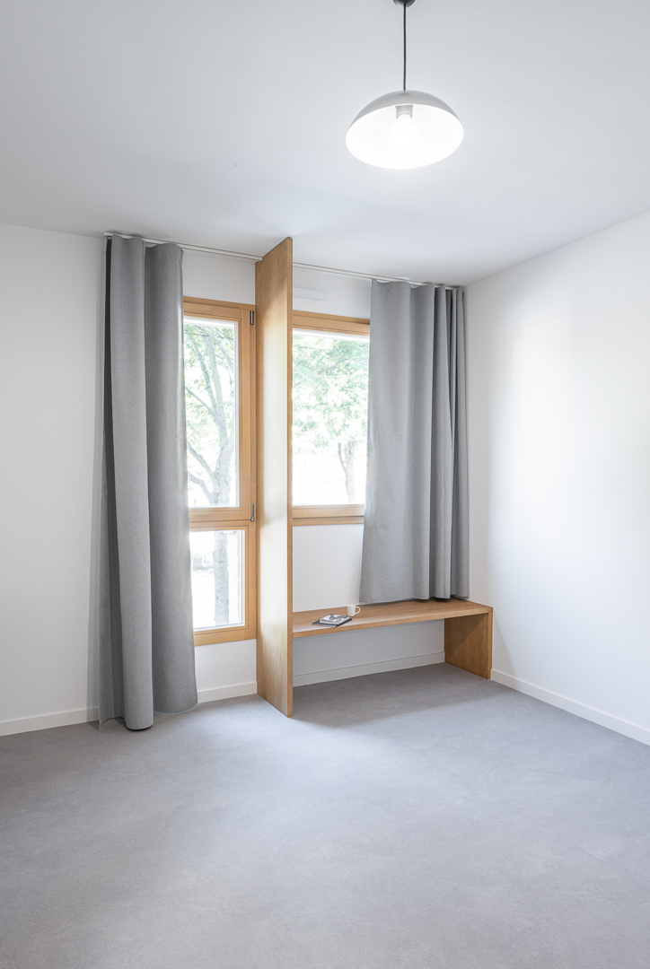 Chambre étudiante avec large double fenêtre en bois et banquette en bois multi usages